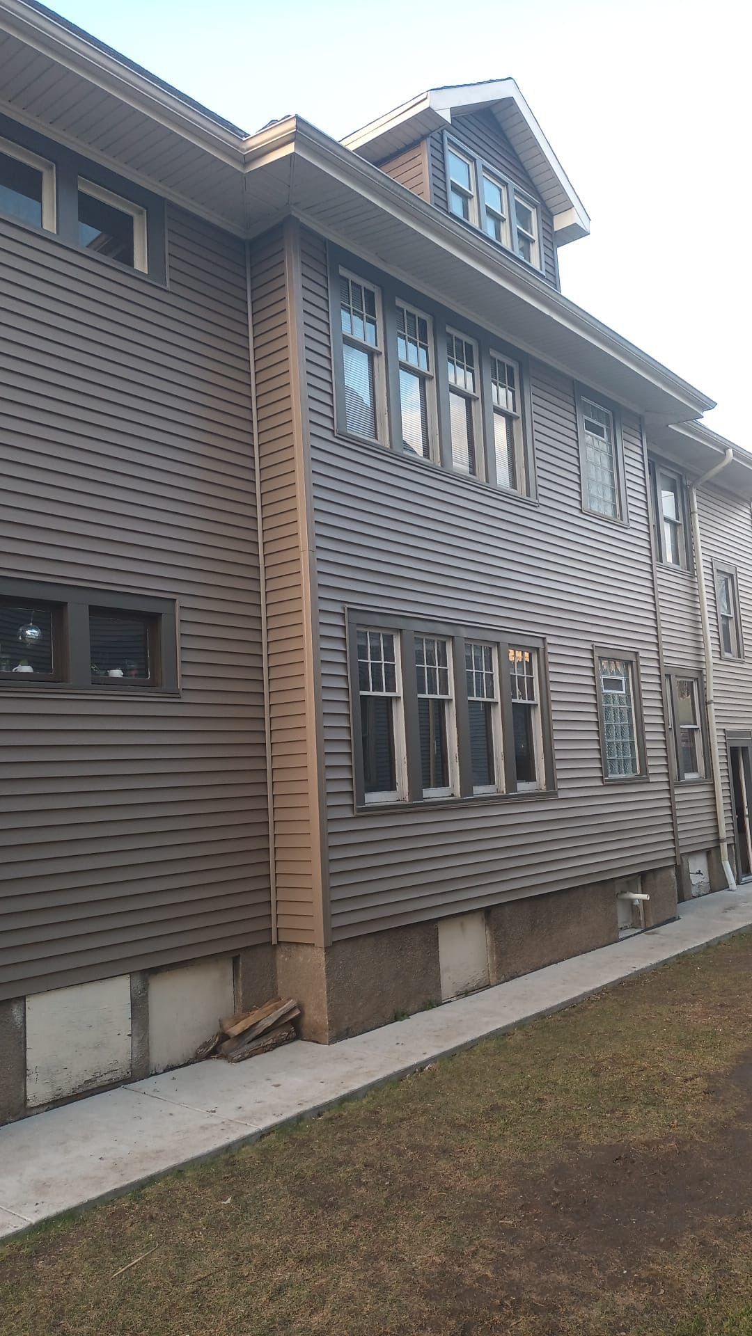 A multi-story brown house with dark siding and multiple windows, viewed from an outdoor angle on a sunny day.