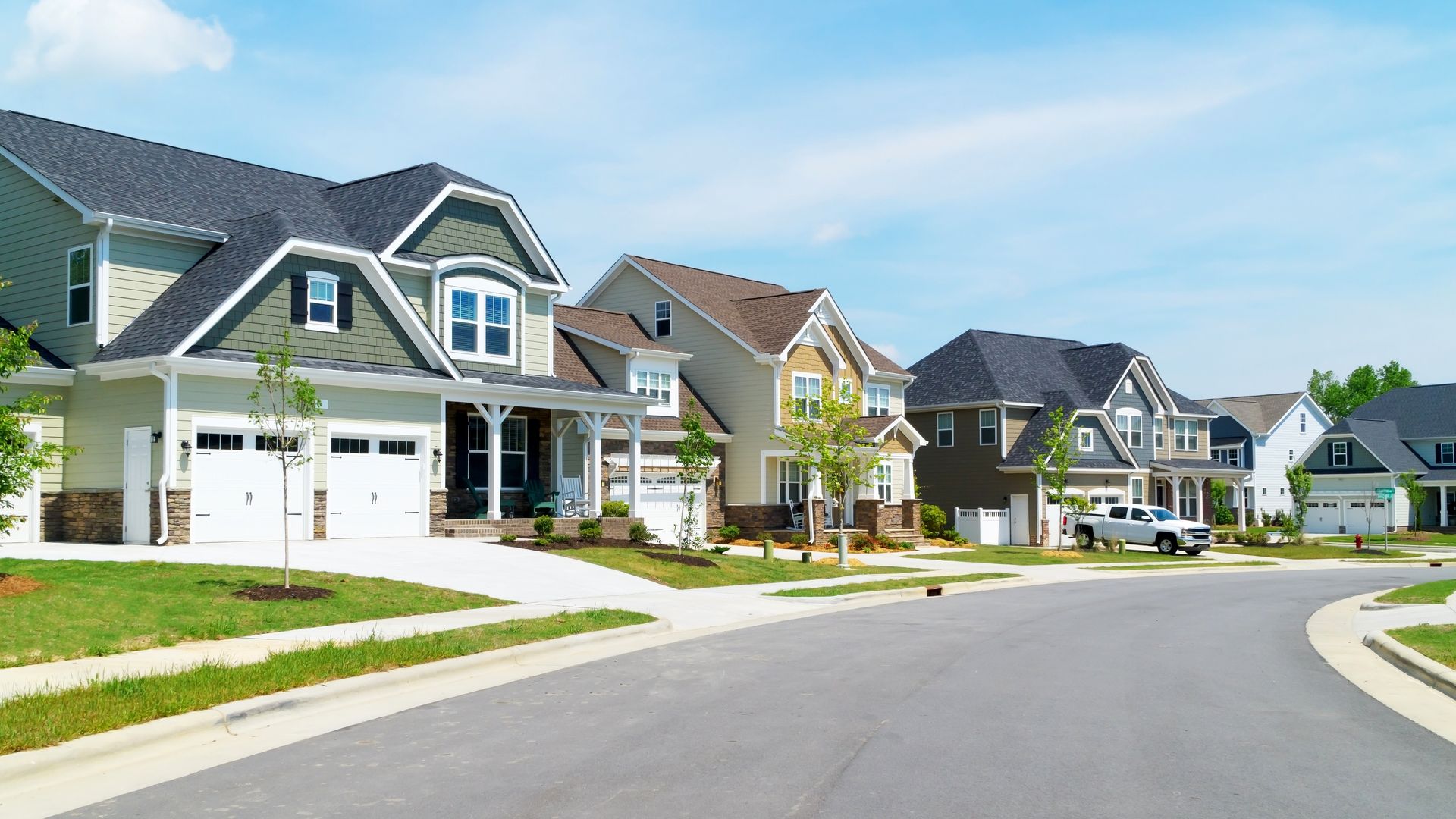 Suburban neighborhood street with modern houses, manicured lawns, and a curving road under a clear sky