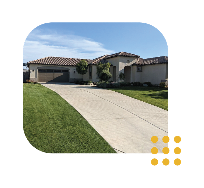 A single-story suburban house with a tan stucco exterior, a tile roof, a multi-car garage, and a long concrete driveway.