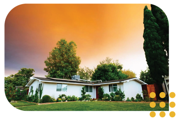 A single-story white house surrounded by trees under a dramatic, orange-hued sunset sky.