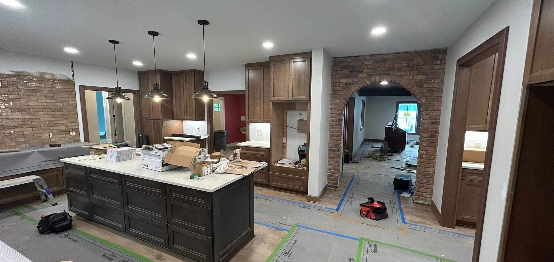 Kitchen undergoing renovation with dark cabinets, a brick archway, and an island.