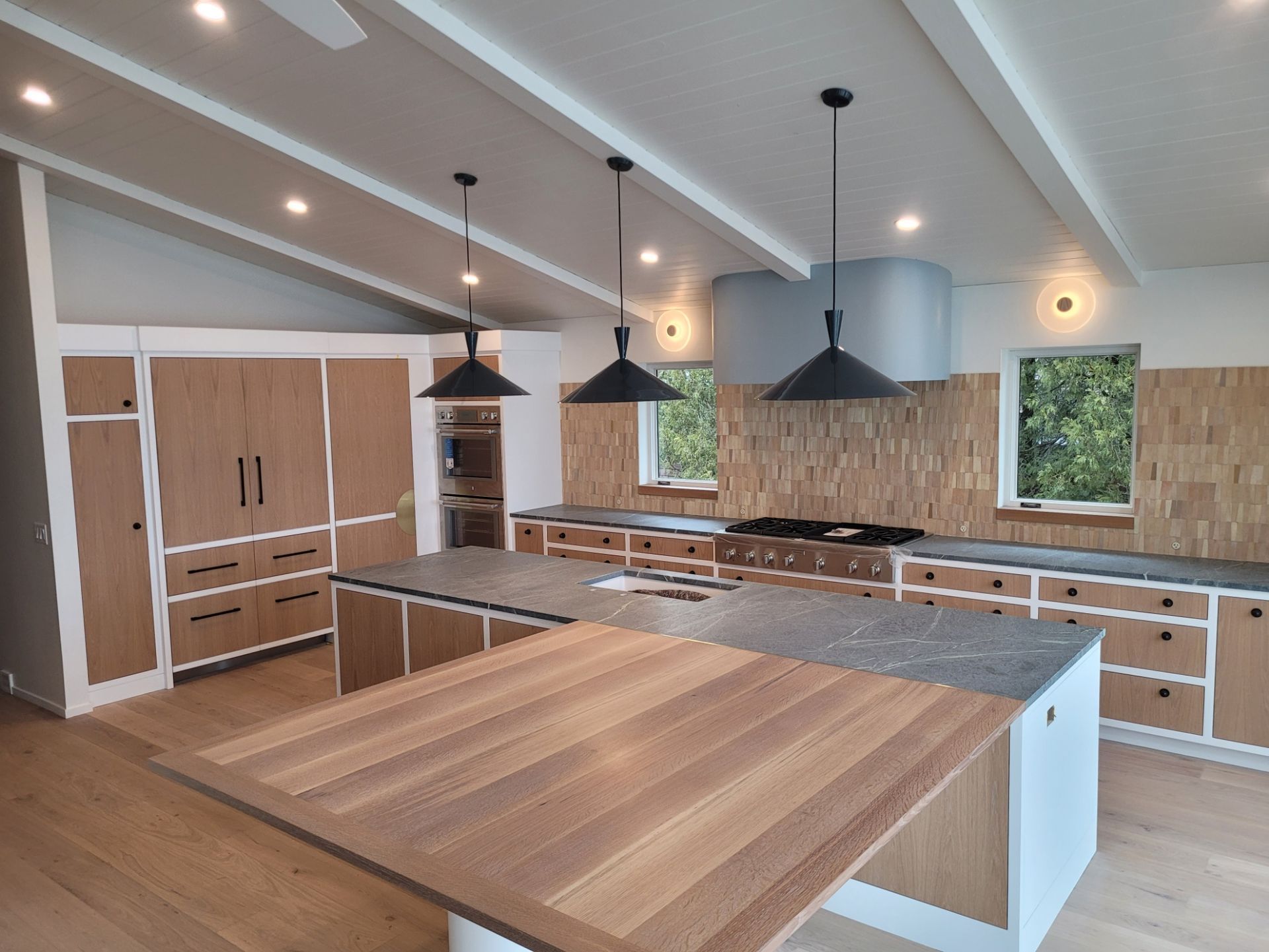Modern kitchen with wooden cabinets, island, and black pendant lights.