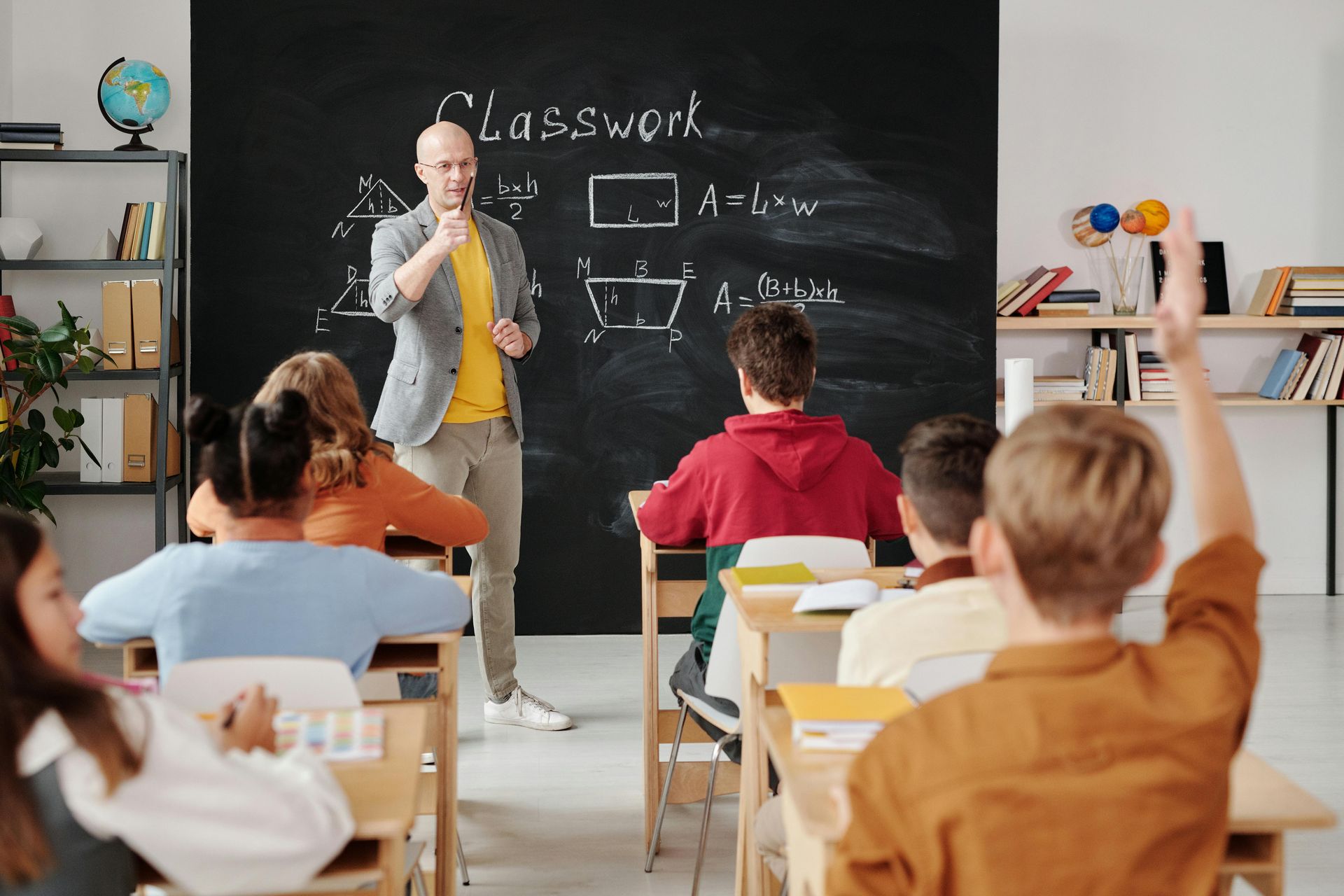Teacher lecturing students in a classroom; student raises hand.