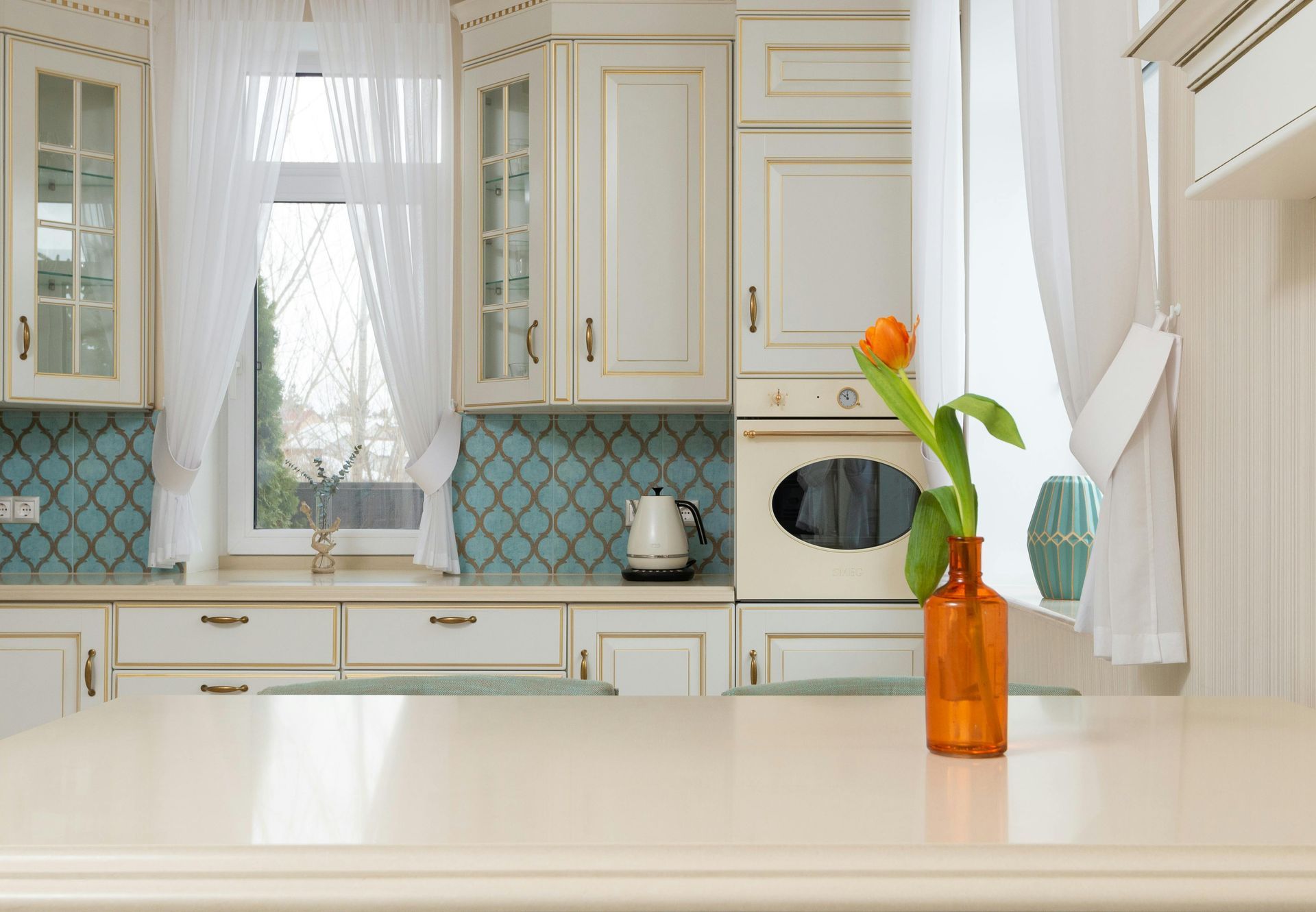 Creamy kitchen with turquoise backsplash, orange flower in a vase on the counter.