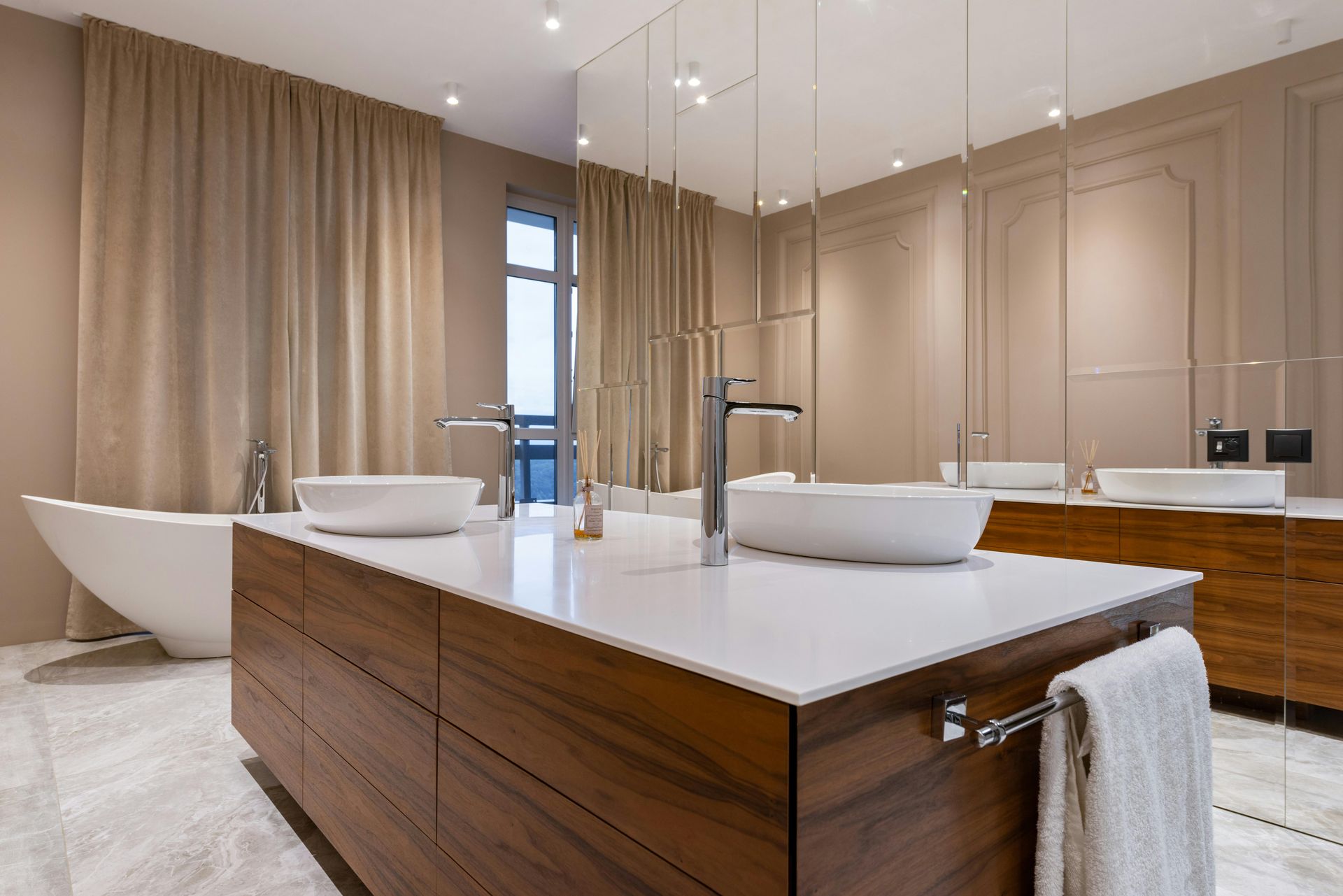 Luxurious bathroom with double sink island, bathtub, mirrors, tan walls, and light marble floor.