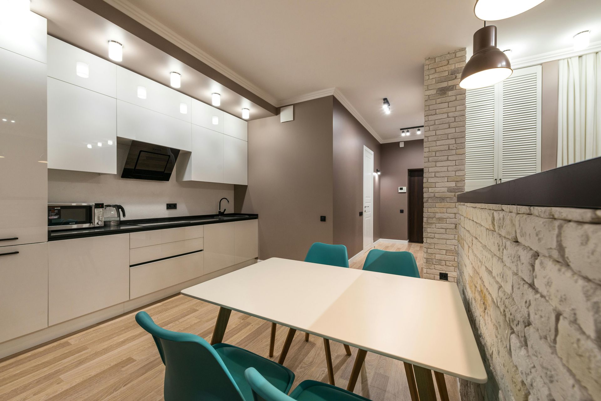 Modern kitchen with white cabinets, teal chairs, and a white dining table.