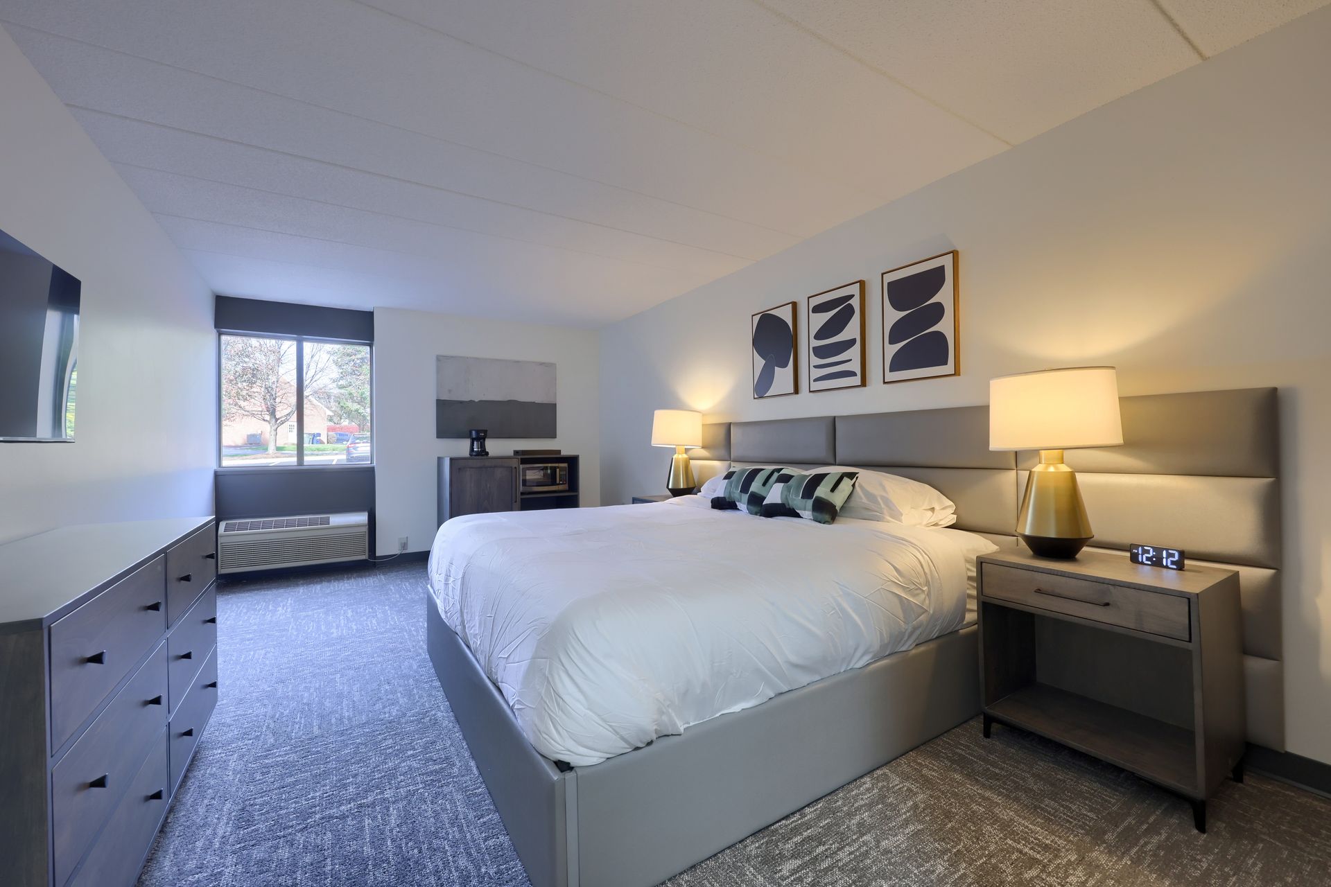 A hotel room with a king size bed , dresser , nightstand and television.