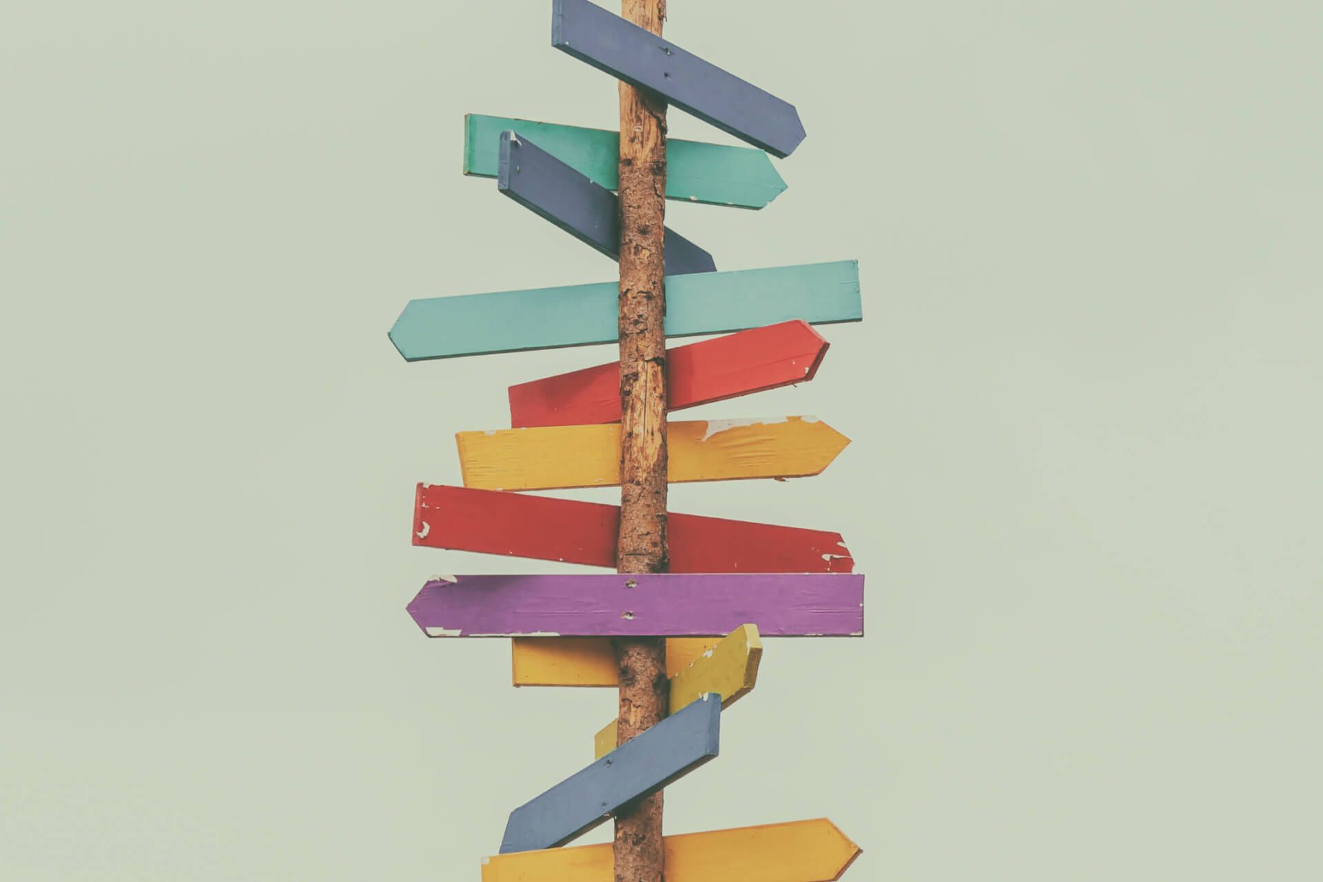 A wooden pole with a bunch of colorful arrows pointing in different directions.