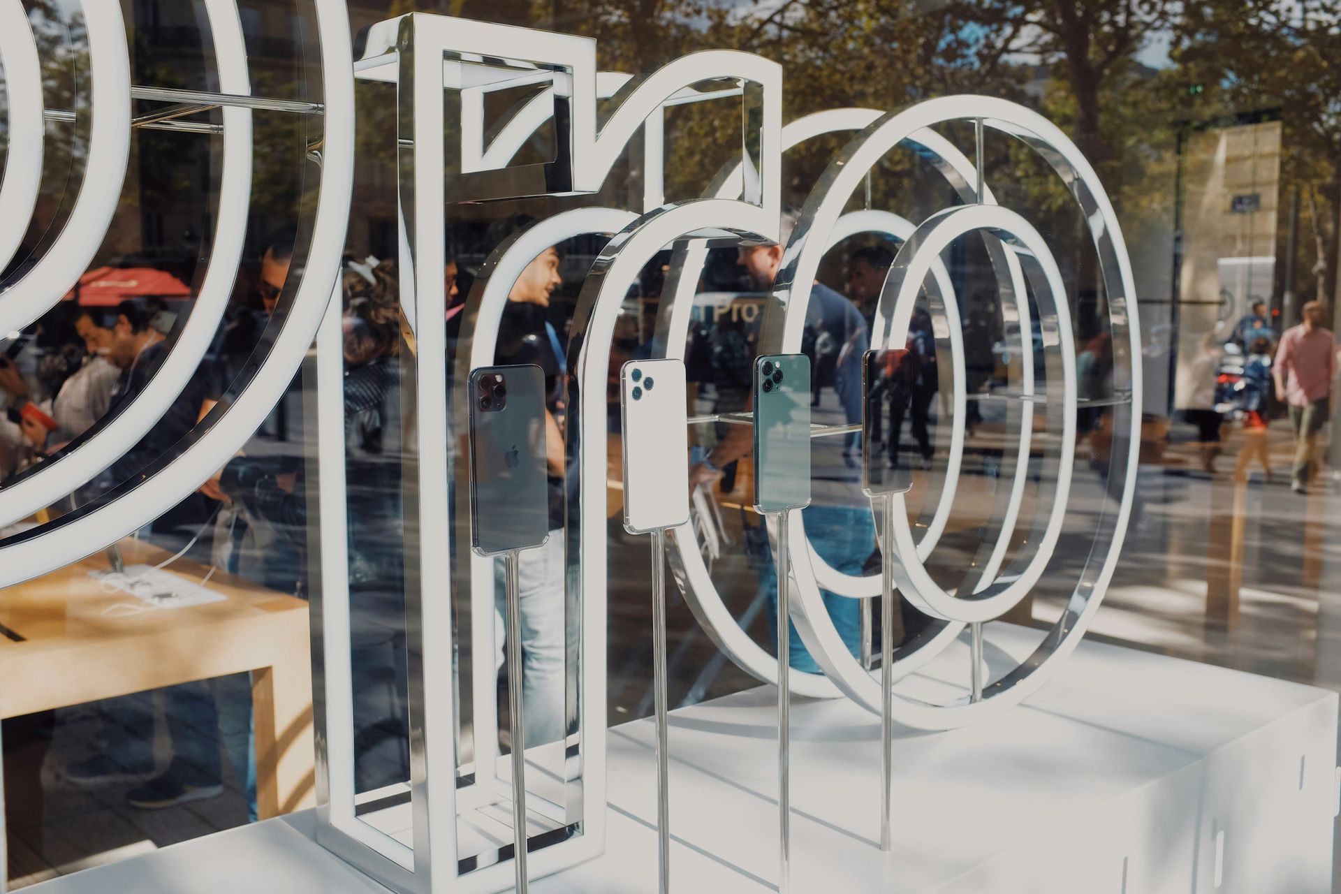 A window display shows four Apple iPhones whilst staff connect with customers inside