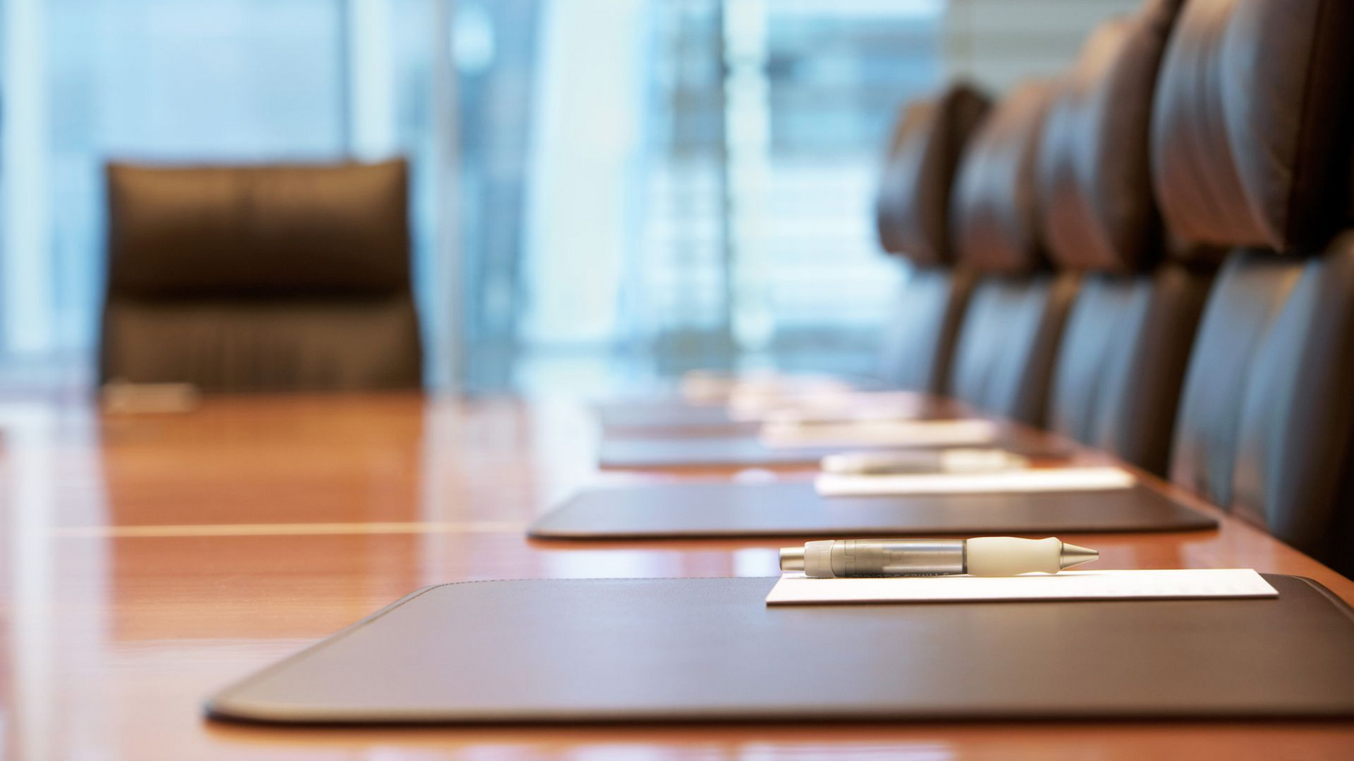 Conference room with leather chairs and a long wooden table. Papers and a pen rest on the table.