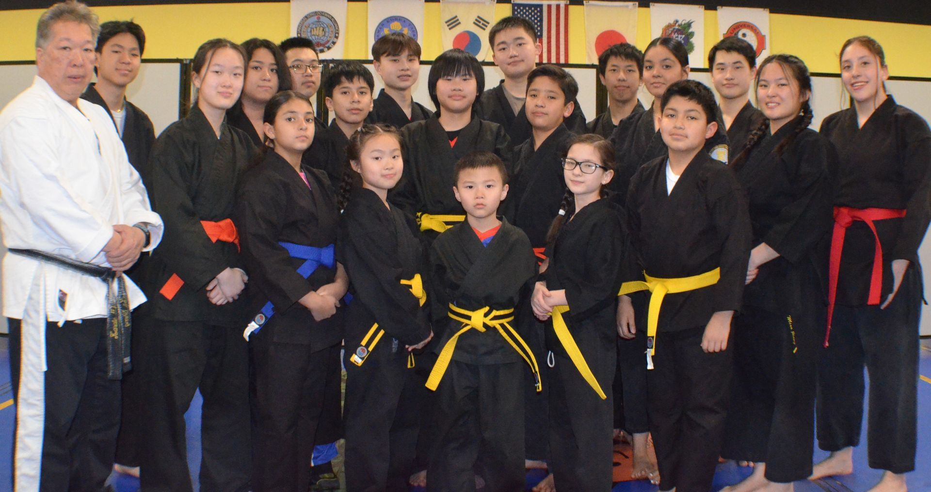 Group of martial arts students and instructors in black uniforms with colored belts posing indoors