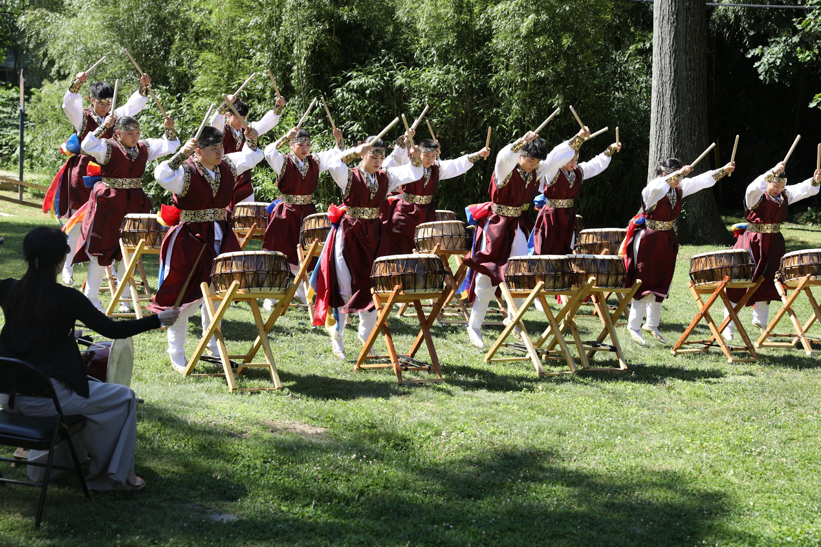 Outdoor folk dance performance in red-and-white costumes with raised arms in a grassy park area