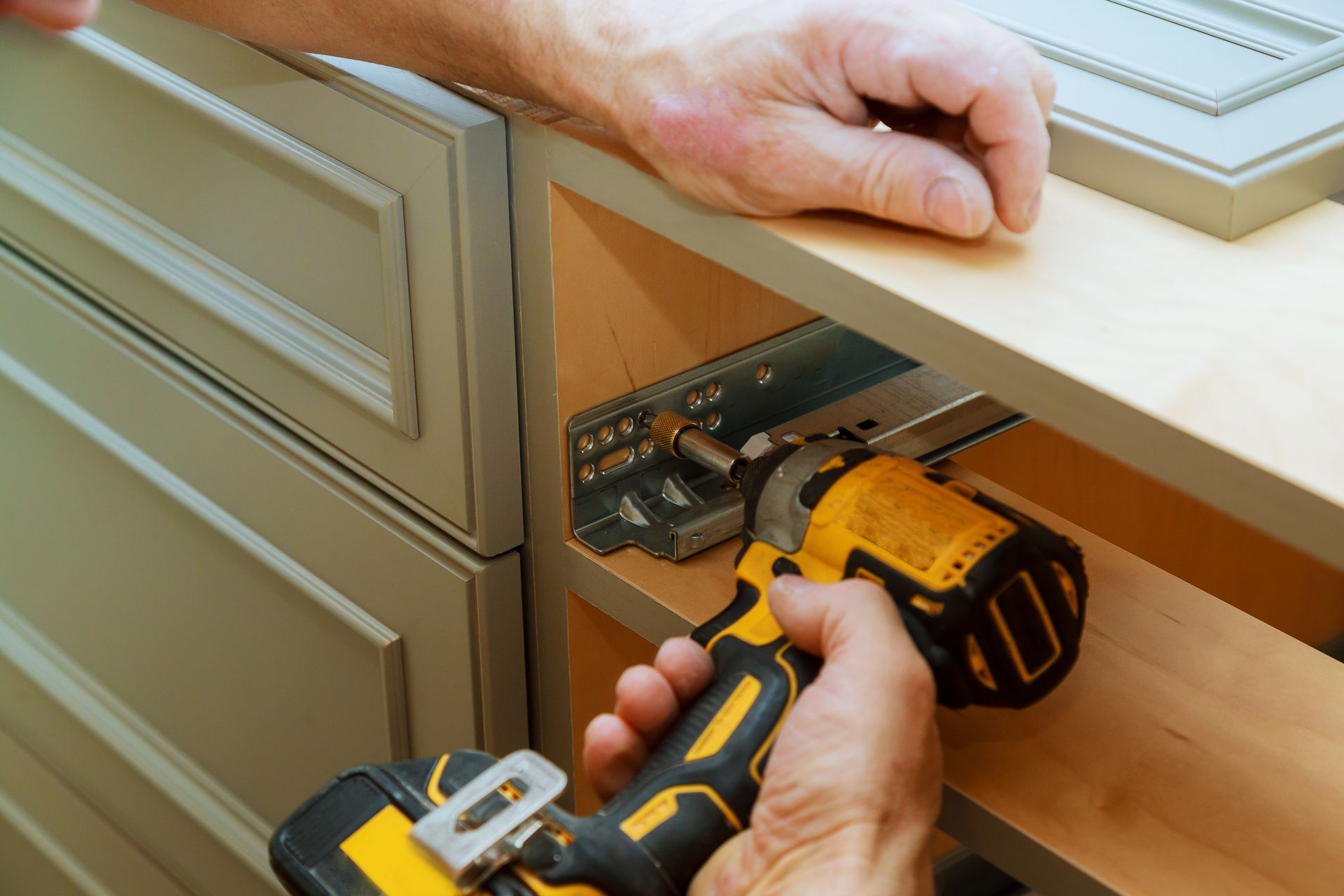 A person installing a cabinet drawer slide with a yellow and black power drill in a kitchen.