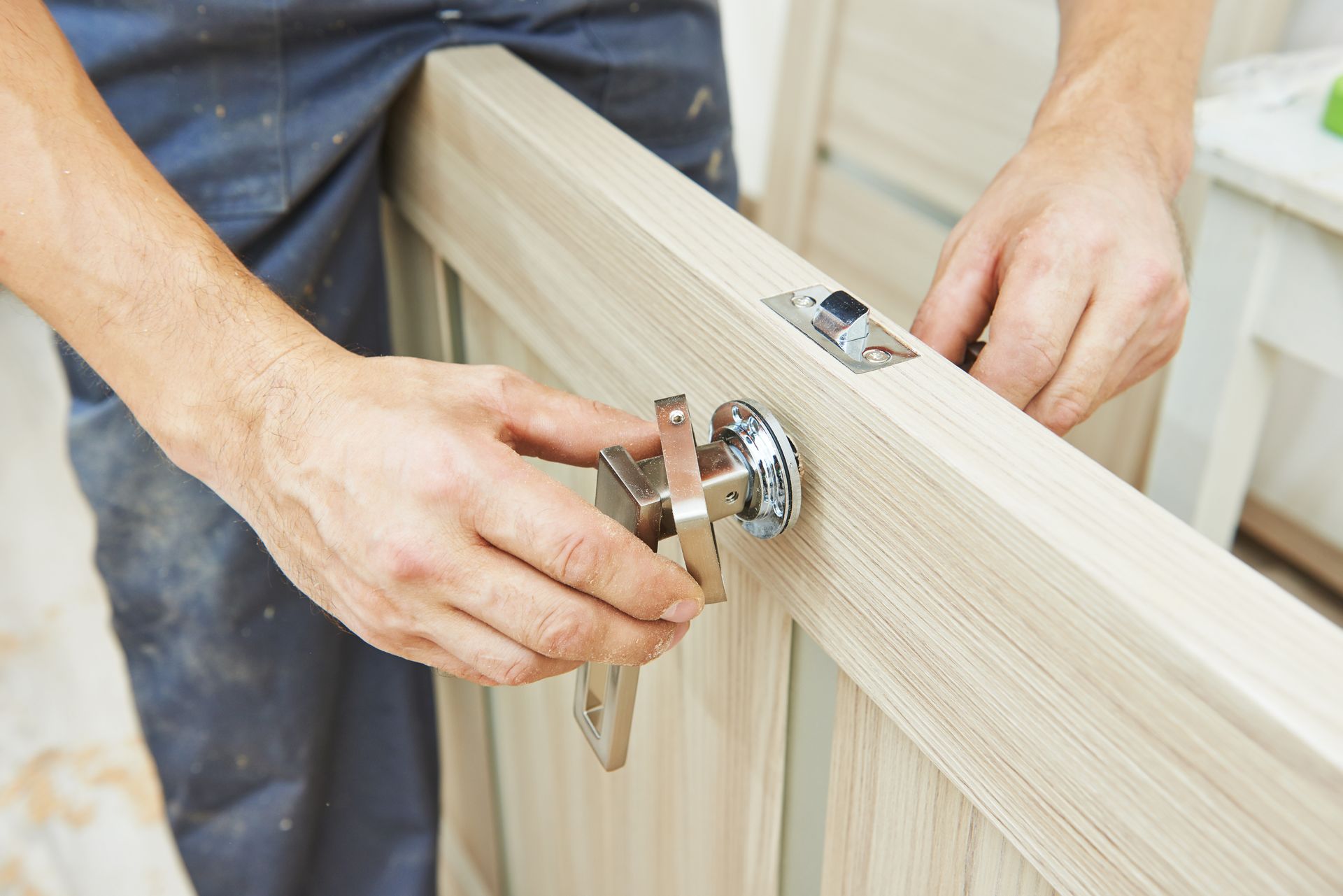 Person installing door handle on a light wooden door; indoor setting.