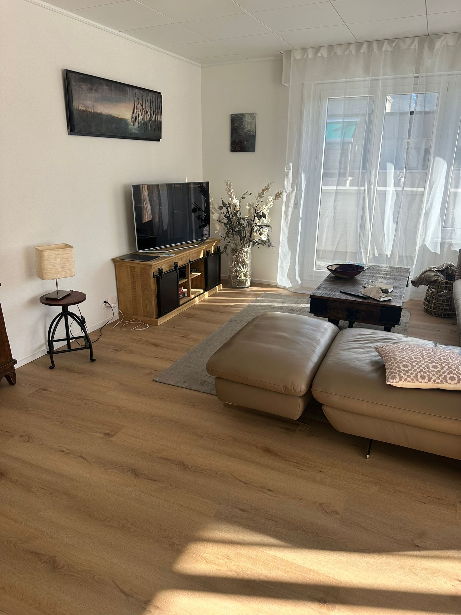 Un salon avec un canapé, une table basse, une télévision et une grande fenêtre.