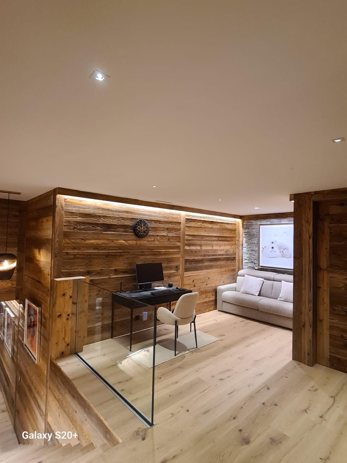Un salon avec des murs en bois et un bureau avec un ordinateur dessus.