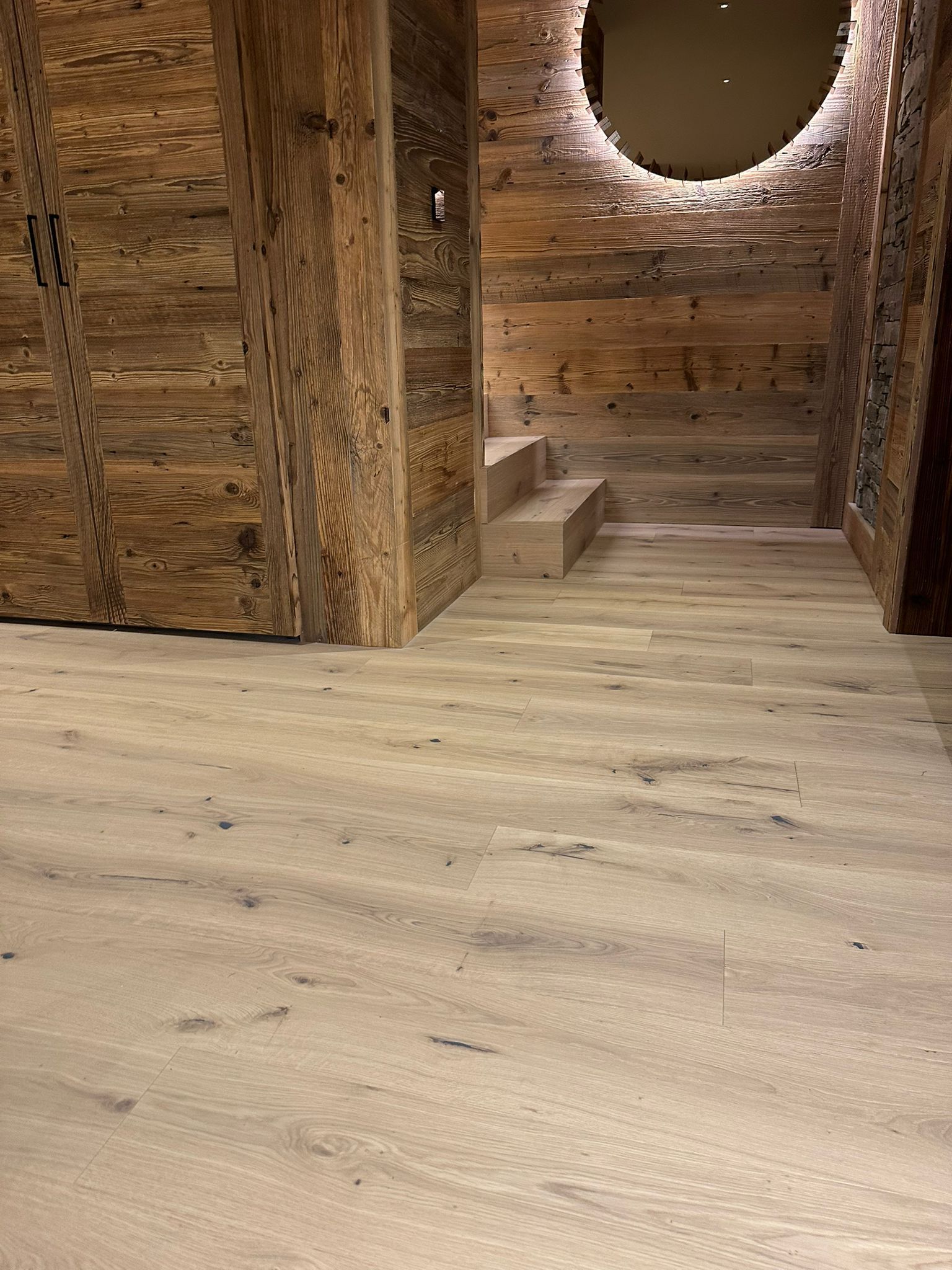 Un couloir avec un mur et des escaliers en bois et un miroir.