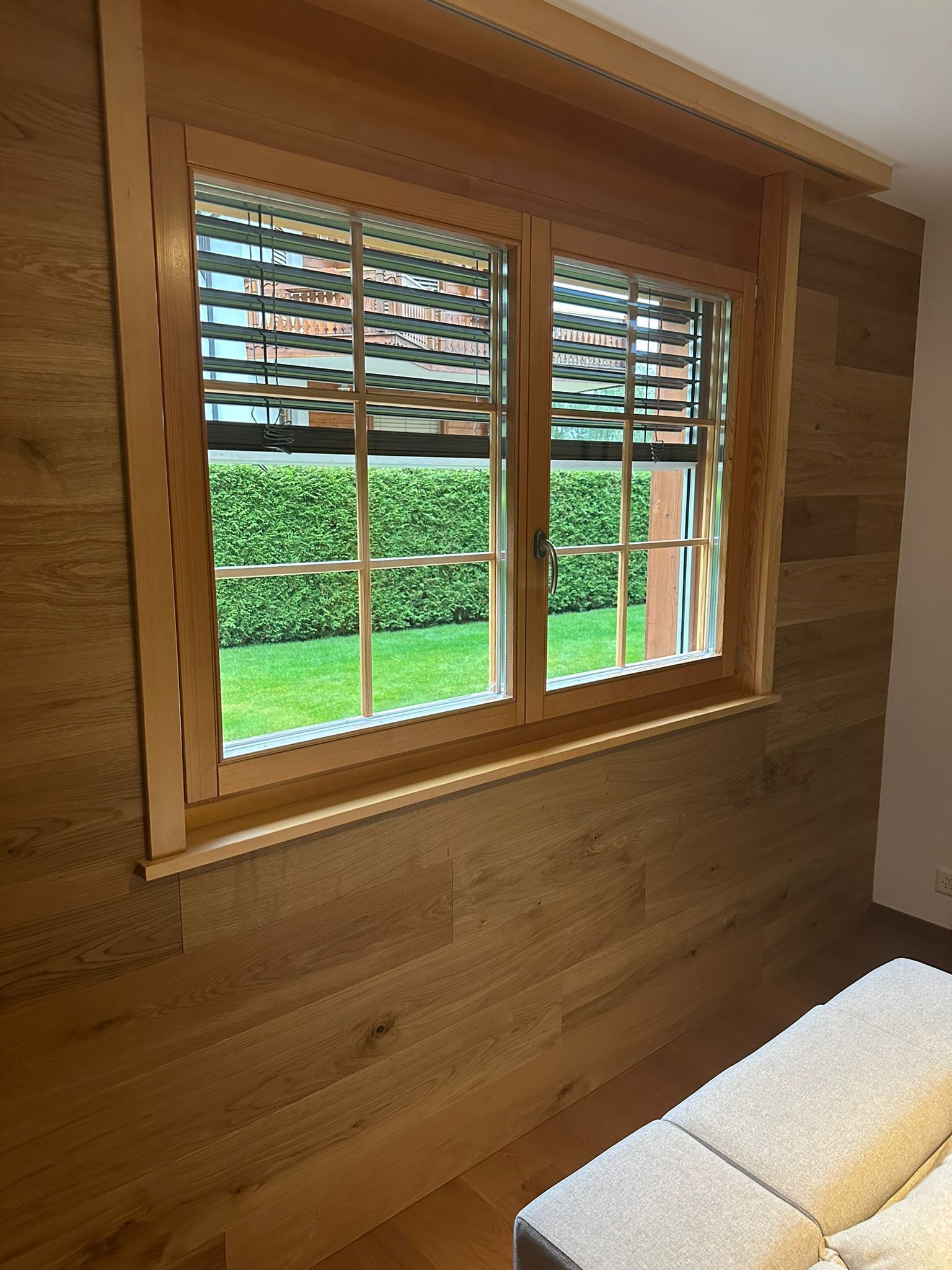 Un salon avec un mur en bois et une grande fenêtre avec stores.