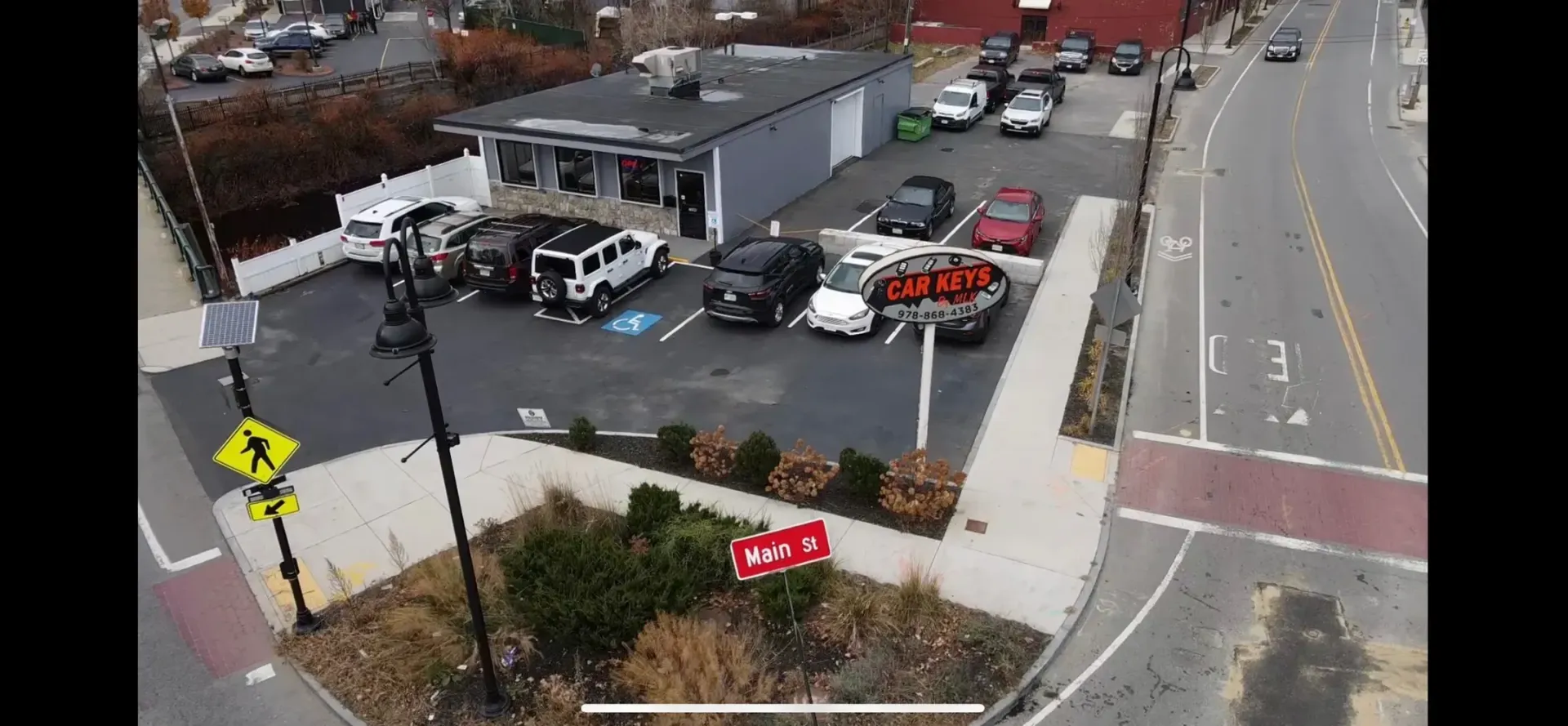 Aerial view of a parking lot beside a road, with several cars and a small building.