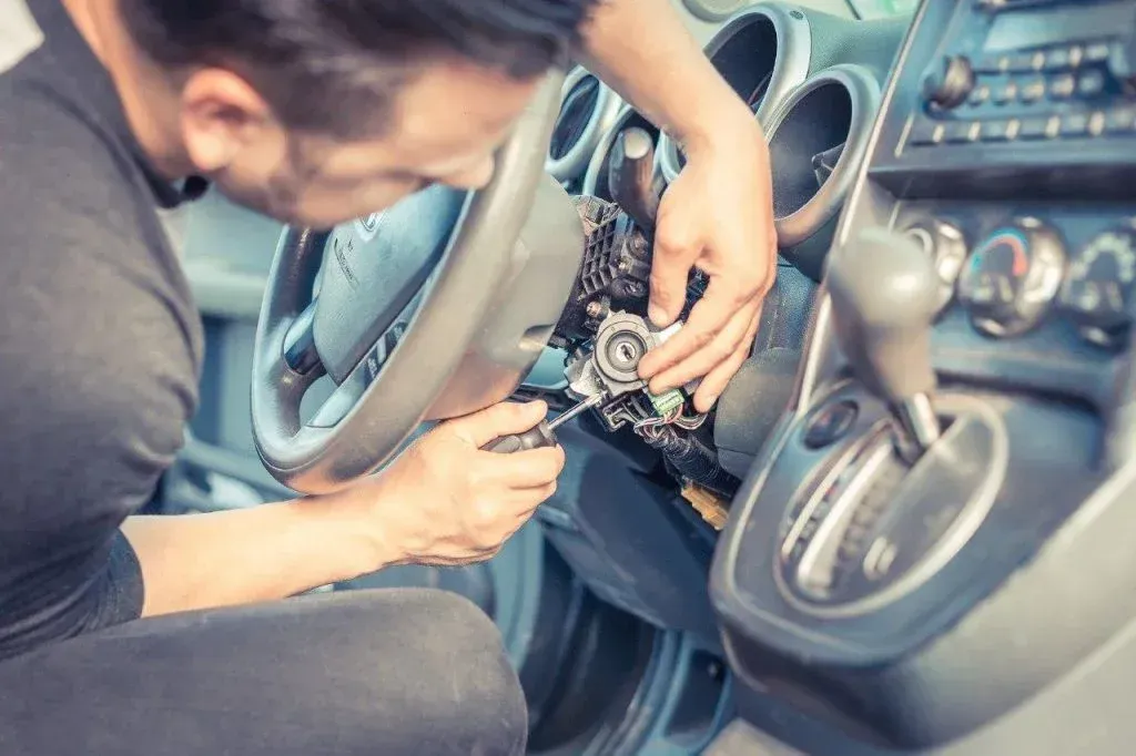 Person repairing the steering column inside a car, using tools near the dashboard.