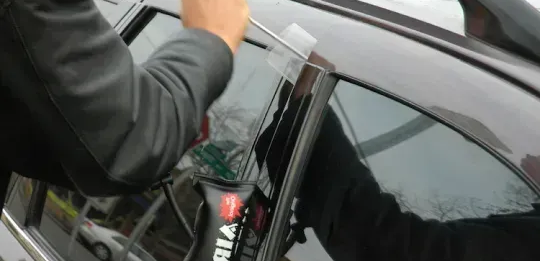Person installing a clear protective film on a car window with a squeegee