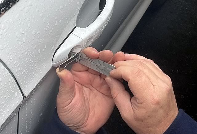 Hands use a key tool to open a silver car door handle on a rainy day
