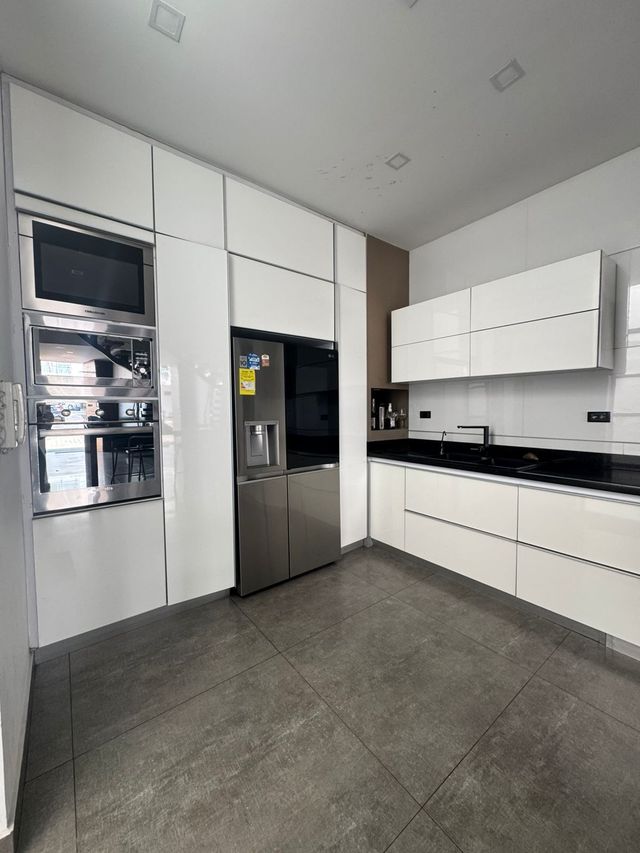 Cocina blanca moderna con electrodomésticos de acero inoxidable, gabinetes y piso de baldosas grises.