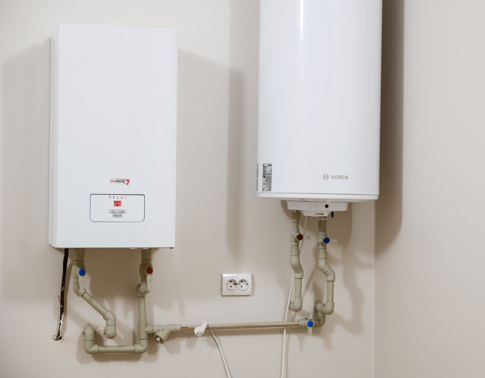 Two water heaters are hanging on a wall next to each other.