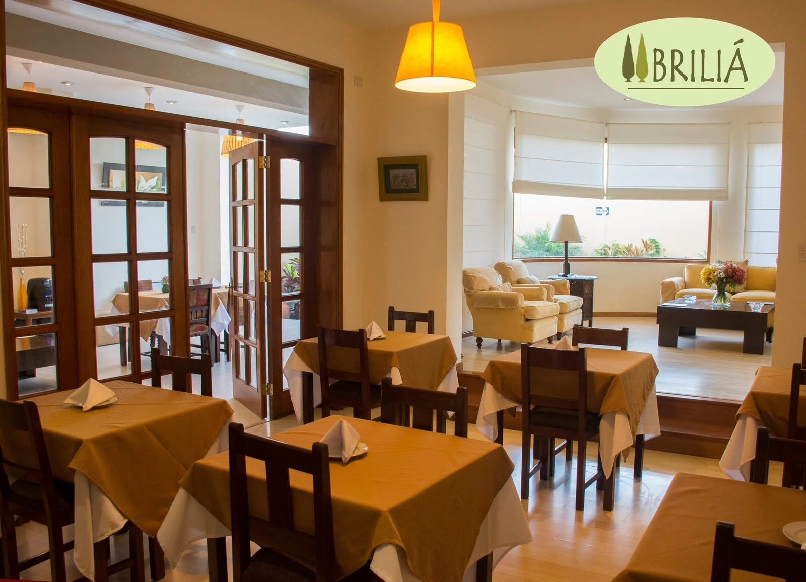 Comedor vacío de un restaurante con mesas de madera, iluminación cálida y un letrero de BRILIA en la pared.