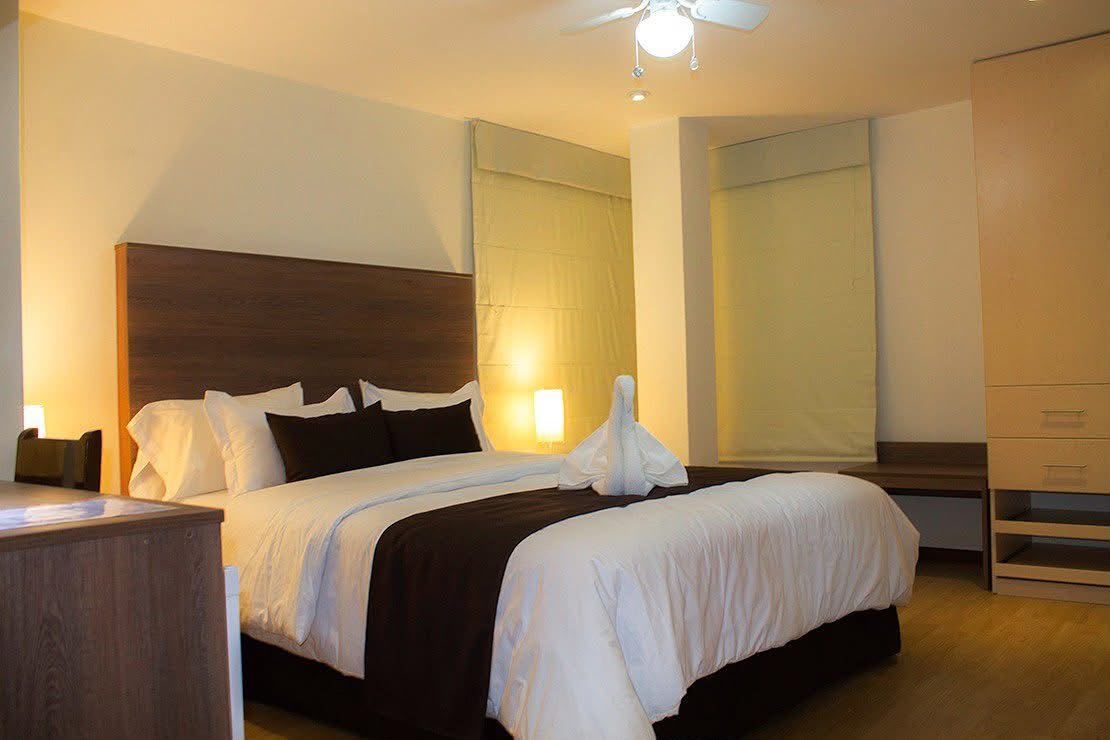 Habitación de hotel con una cama bien hecha, cabecero de madera e iluminación cálida.