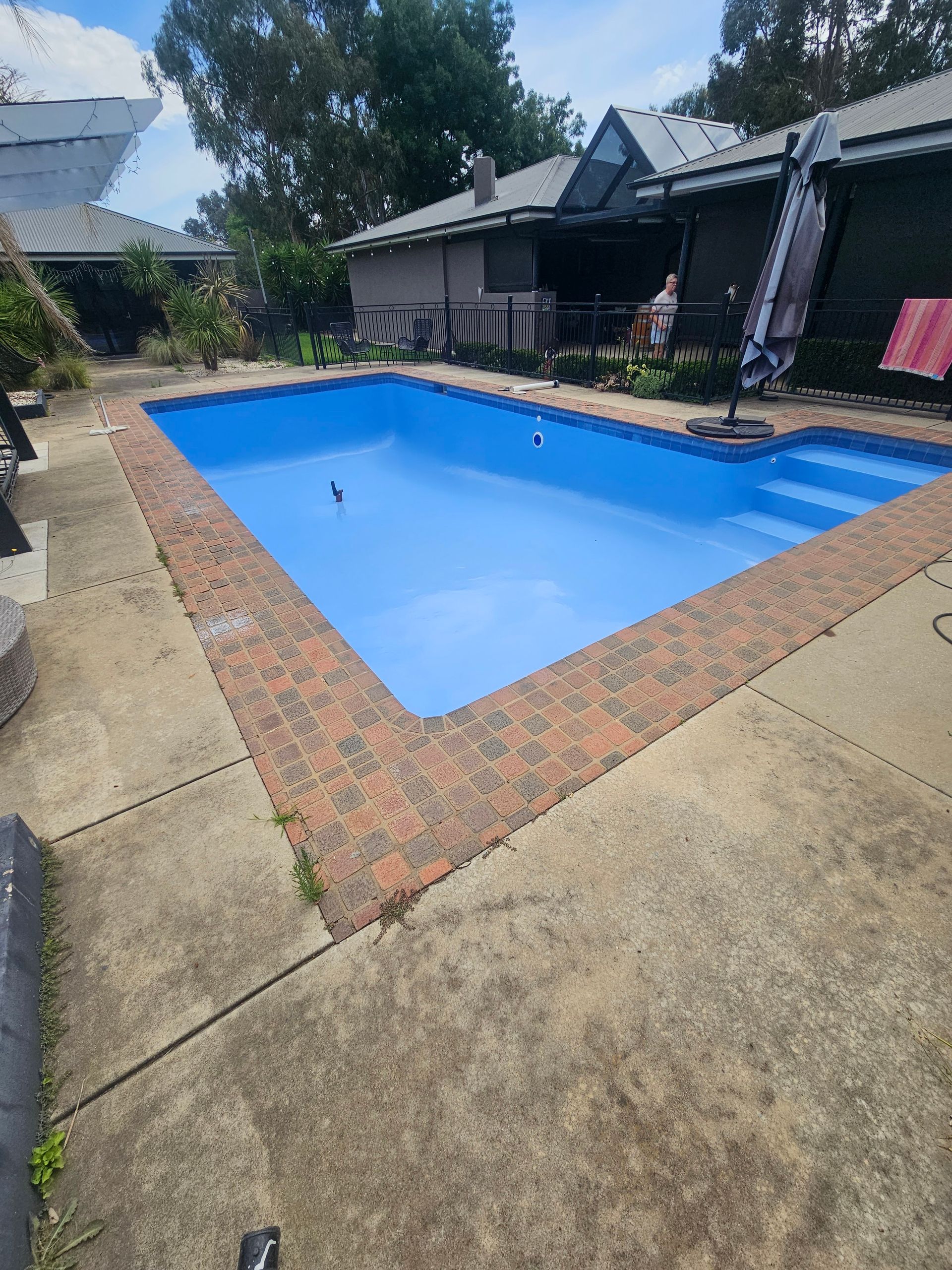 A blue-painted swimming pool surrounded by a brick border and concrete patio — Riverina Epoxy Flooring In Glenfield Park, NSW