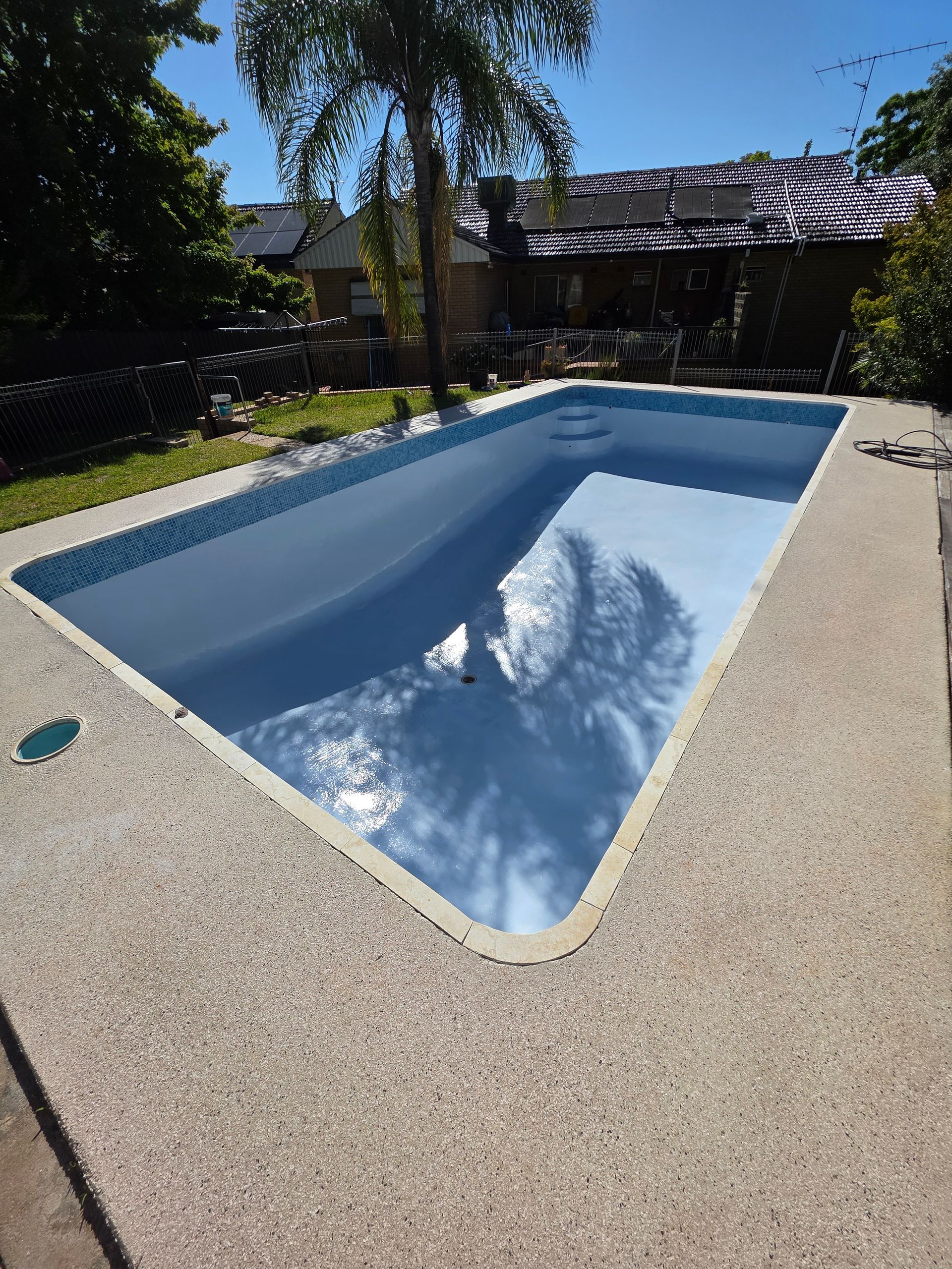 Rectangular swimming pool with light blue water, surrounded by speckled concrete. Sunny outdoor setting — Riverina Epoxy Flooring In Glenfield Park, NSW