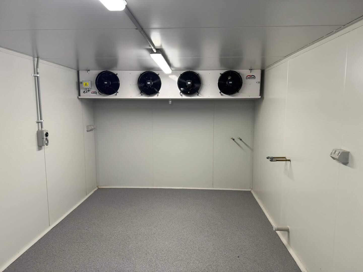Empty white walk-in freezer with a four-fan unit. Gray floor, fluorescent lights, and electrical components — Riverina Epoxy Flooring In Glenfield Park, NSW