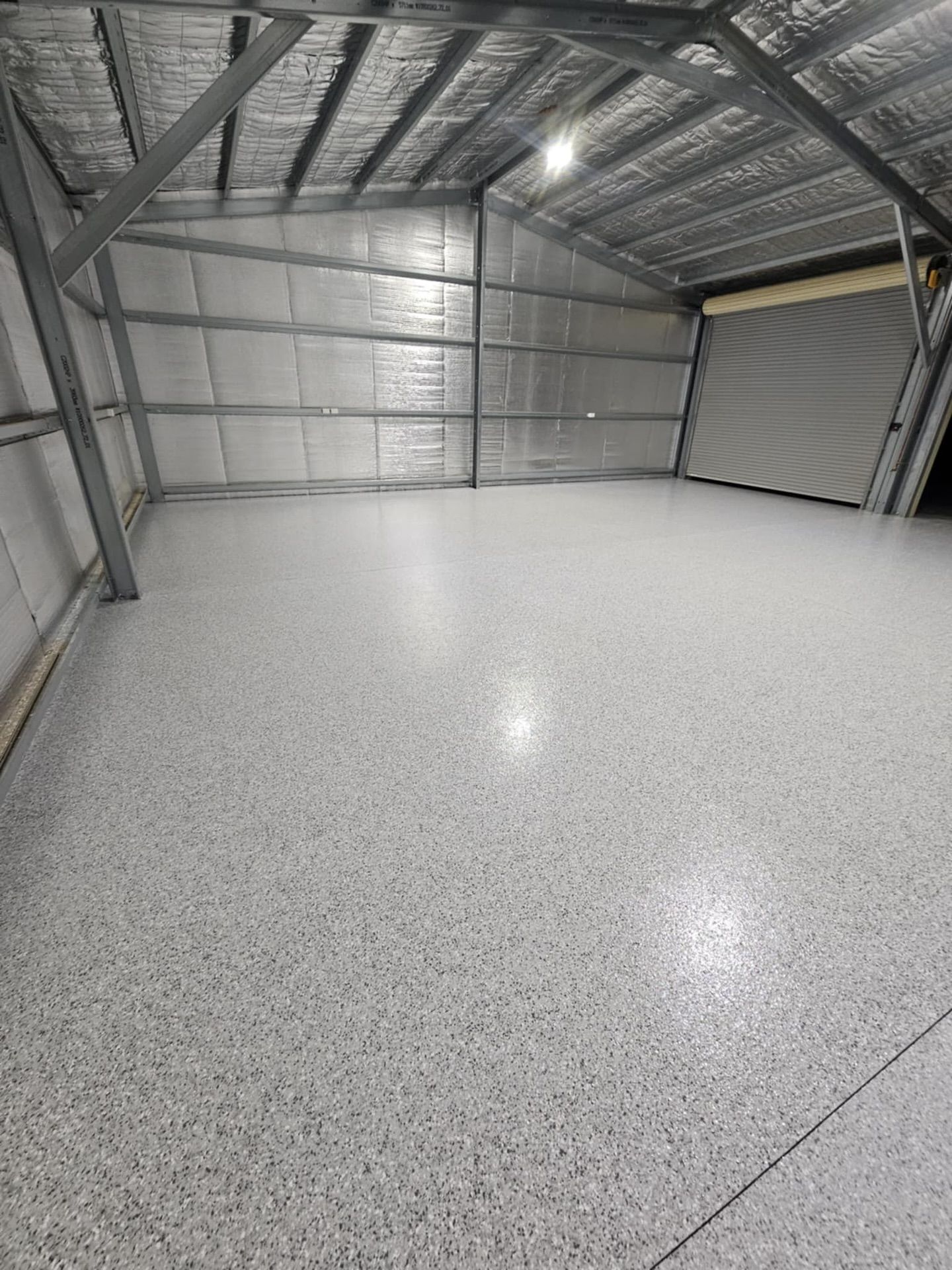 Empty industrial warehouse with gray speckled epoxy flooring and a roll-up door — Riverina Epoxy Flooring In Glenfield Park, NSW