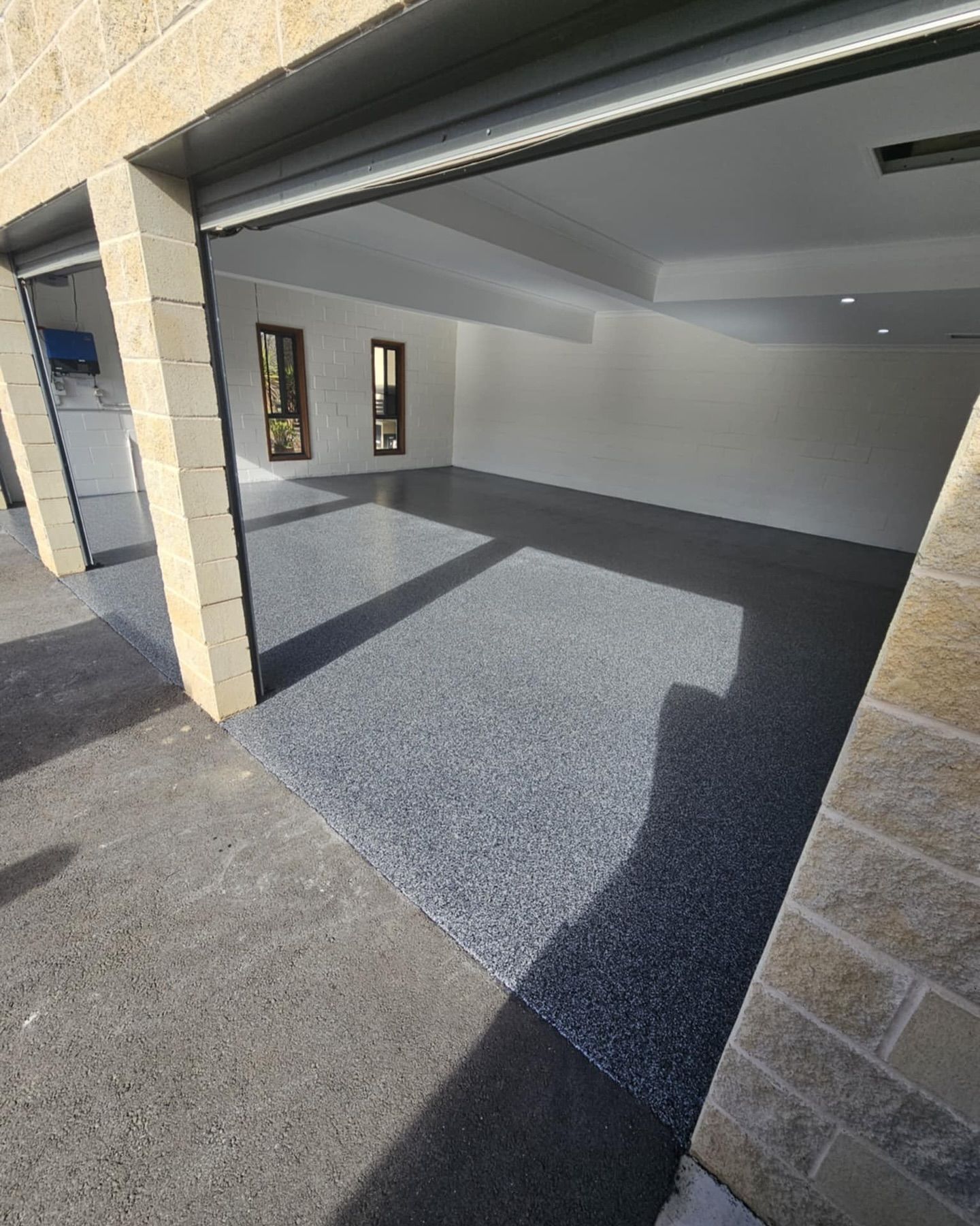Open garage interior with gray speckled flooring, white walls, and two small windows — Riverina Epoxy Flooring In Glenfield Park, NSW