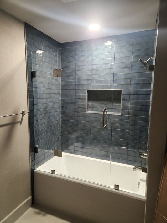 Modern bathroom with white tub, blue tile wall, and chrome shower fixtures