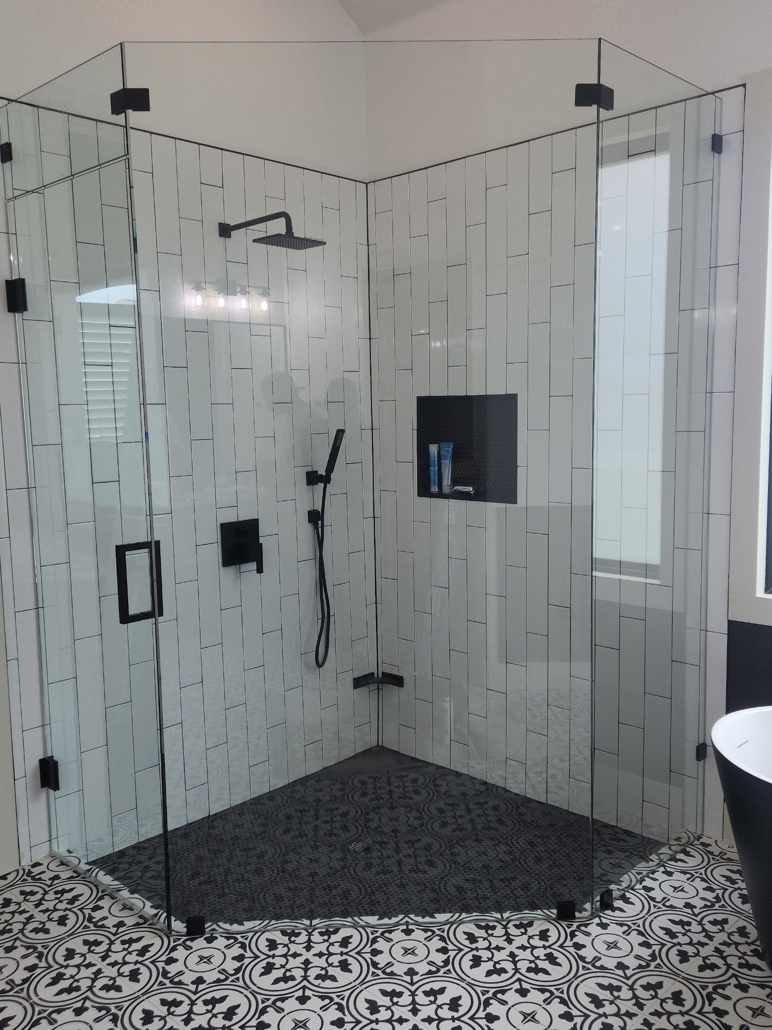 Modern glass shower enclosure with a black shower floor and patterned tile bathroom floor.
