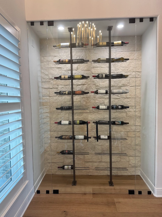 Floor-to-ceiling wine rack display in a narrow room with brick wallpaper and a gold chandelier