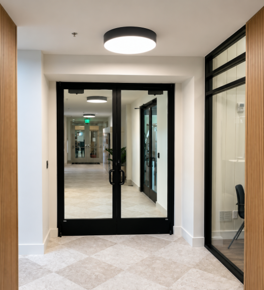 Modern hallway with black-framed glass double doors and office windows on the right.