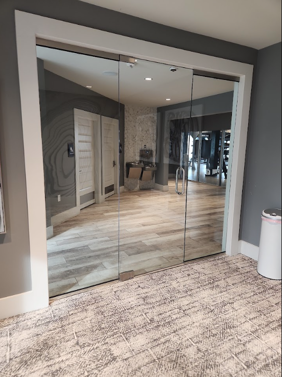 Glass double doors reflecting a modern hallway with wood floors and gray walls