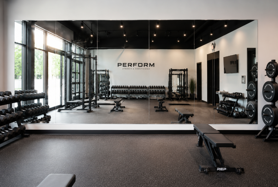 Modern gym interior with dumbbells, benches, mirrors, and large windows