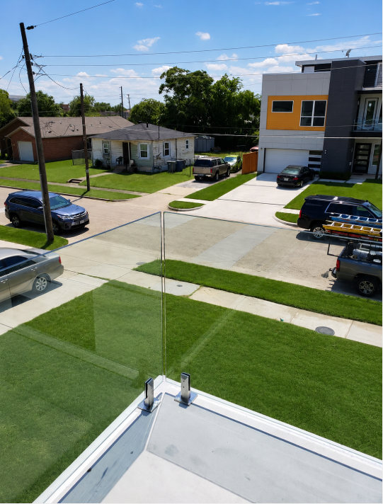 View from a rooftop over a residential street with houses, parked cars, and bright green lawns under a blue sky