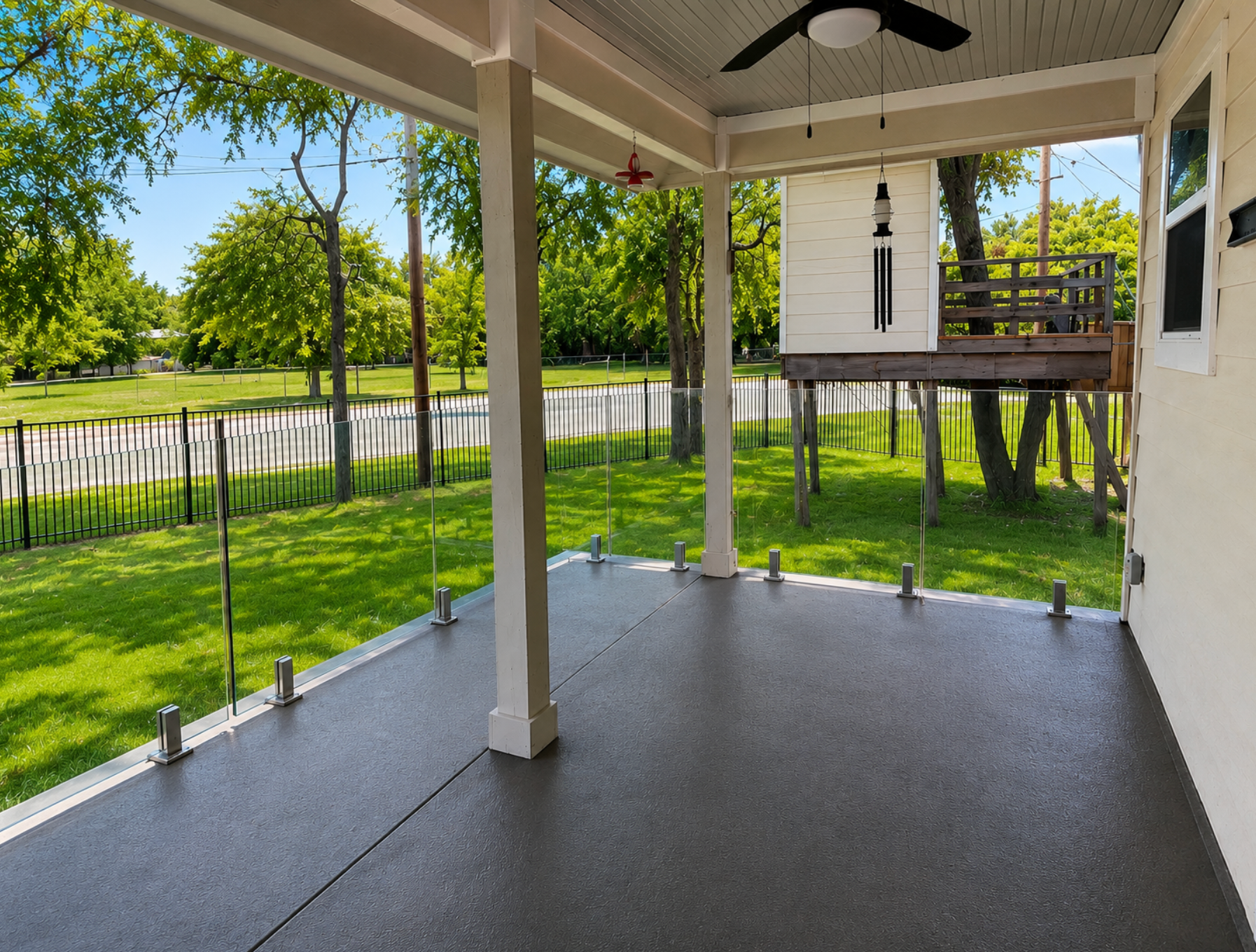 Covered back porch with gray floor, white columns, ceiling fan, and view of green yard and fence.