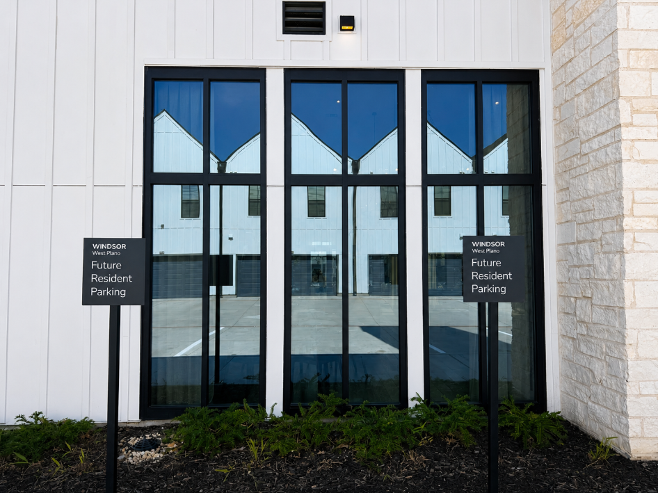 Building entrance with black-framed glass doors and two parking signs beside a stone wall.