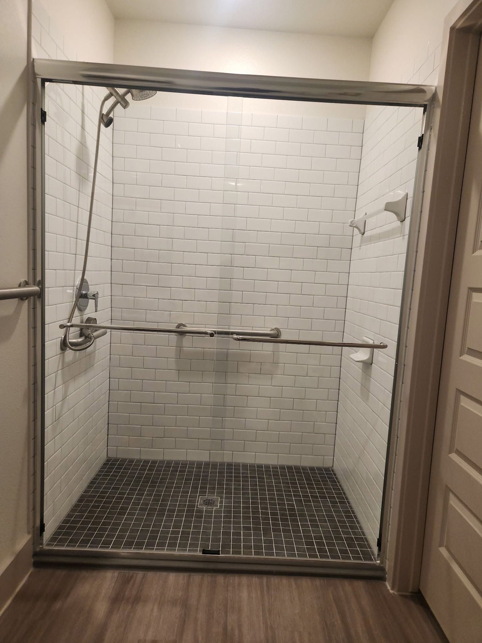 Empty tiled shower with black hex tile floor and glass door frame.
