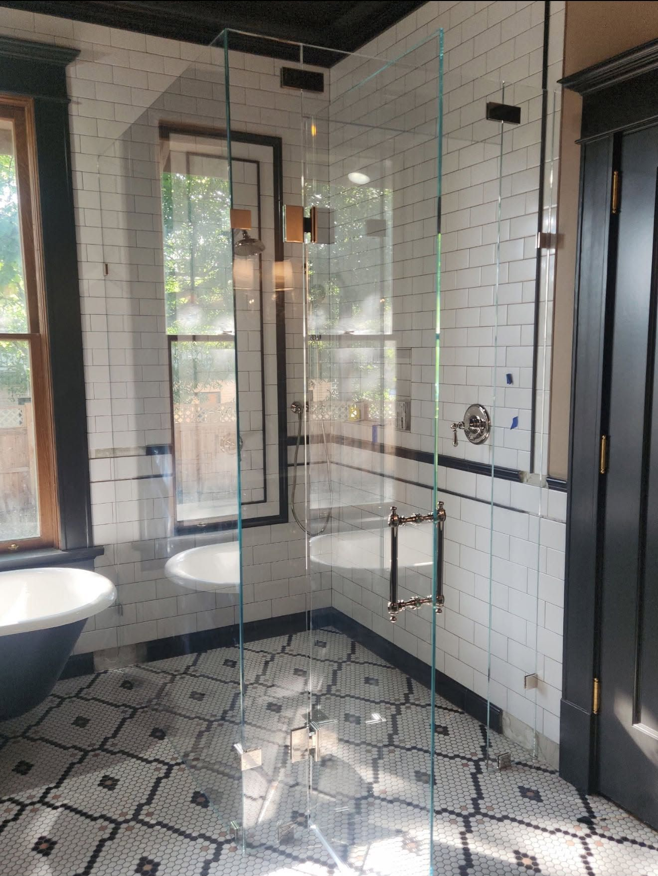 Modern black-and-white bathroom with glass shower, freestanding tub, and patterned tile floor