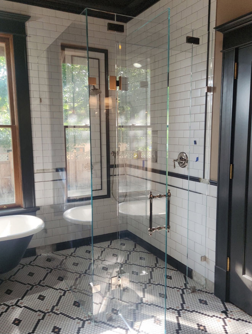 Modern bathroom with glass shower, black-and-white tile, and freestanding tub near a window.