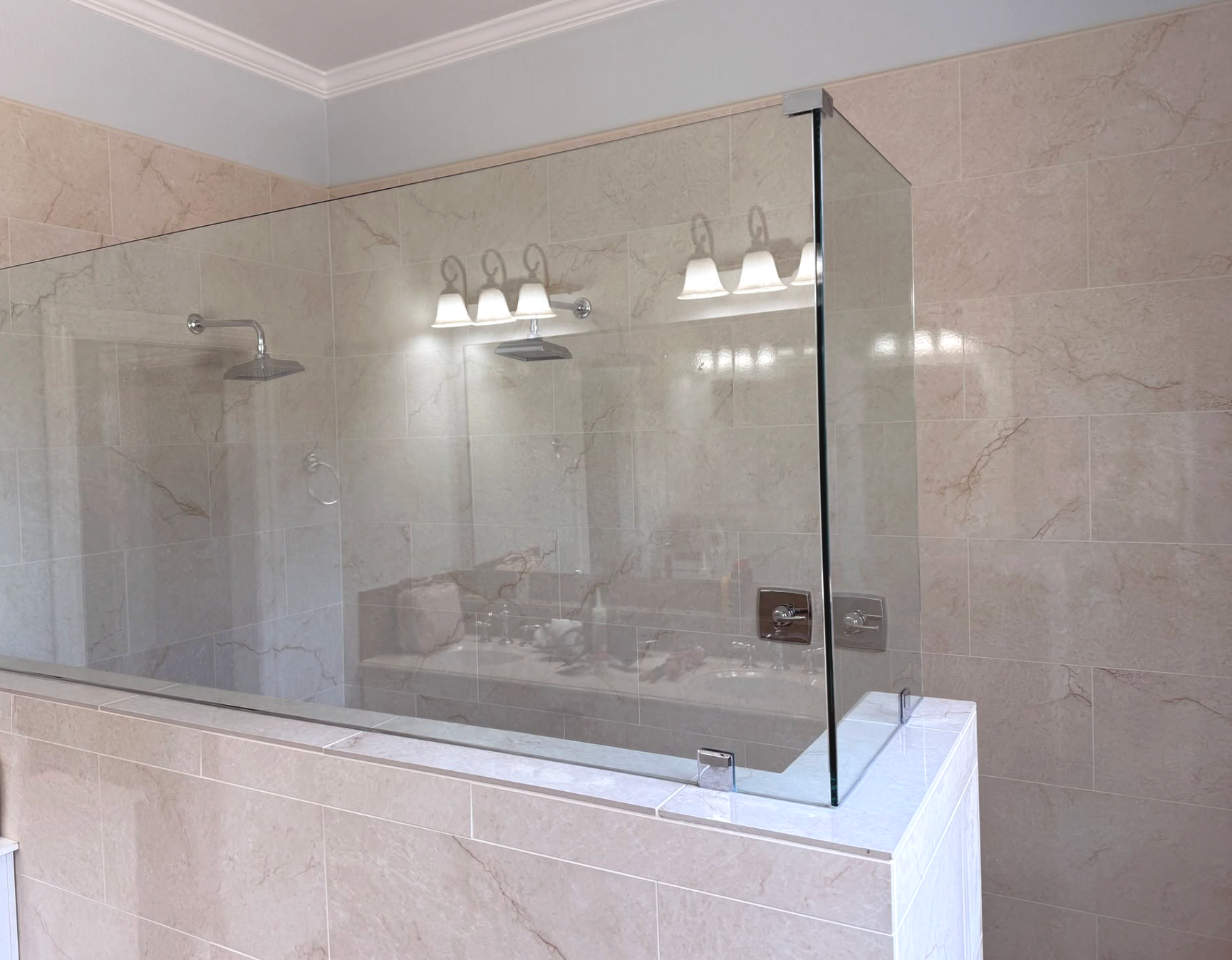 Bathroom with a glass shower enclosure above a tiled bathtub surround and wall-mounted light fixtures.