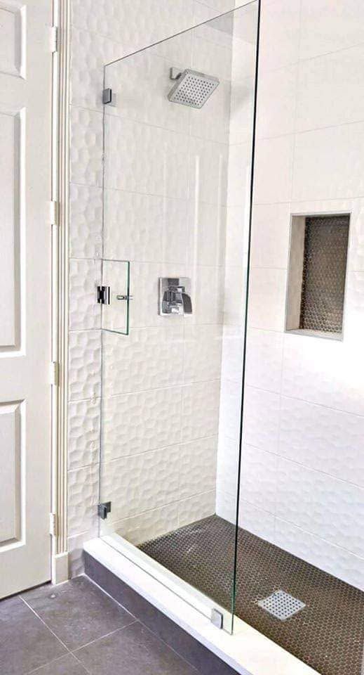 Glass walk-in shower with chrome fixtures, white tiled walls, and dark textured floor.
