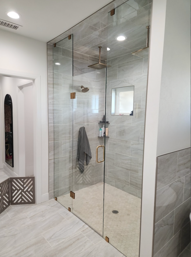 Modern walk-in shower with clear glass doors, white tile, and a towel hanging inside